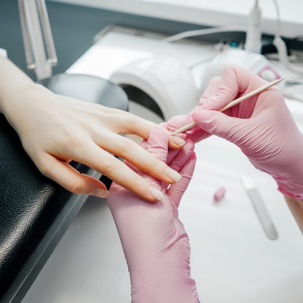 Young woman getting manicure in beauty salon. Manicurist make manicure in pink gloves.